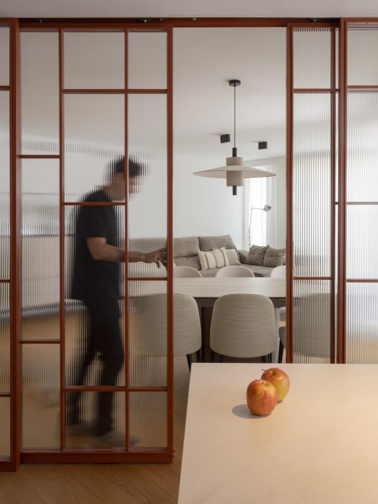 Imagen de la cocina del apartamento desde la que se ve la corredera de vidrio que cierra el espacio al salón comedor.